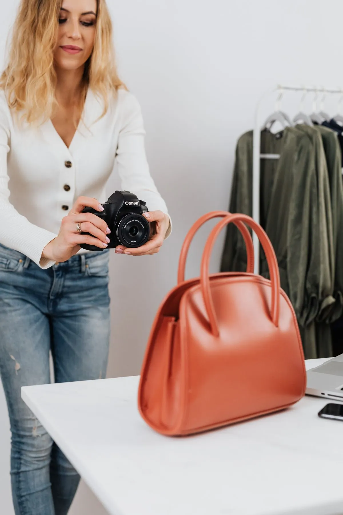 Photographer shooting a handbag product photo in a studio with a clothing rack behind